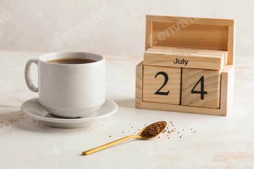 Preview: Instant coffee in a spoon on the background of a coffee mug and a wooden calendar on July 24.