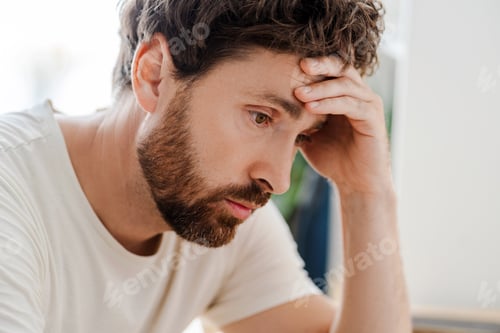 Preview: Thoughtful pensive young male sitting at home, close up