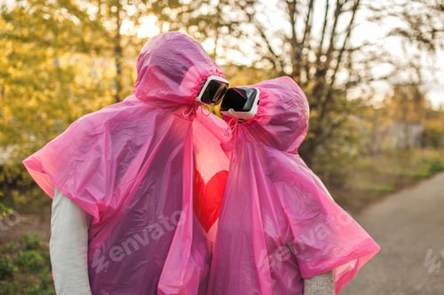 Preview: Two people romantically looking at each other in pink plastic raincoats and VR headset