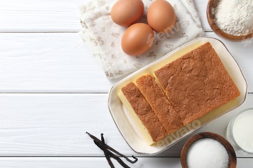 Preview: Tasty Japanese Castella sponge cake and ingredients on white wooden table, flat lay. Space for text