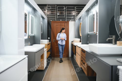 Preview: Young woman choosing new bathroom furniture at the plumbing shop with lots of sanitary goods