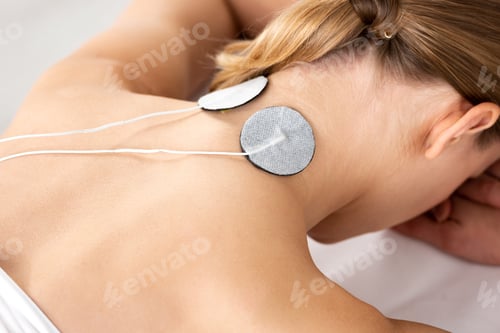 Preview: Back view of young woman with electro stimulation electrodes on neck on massage couch isolated on