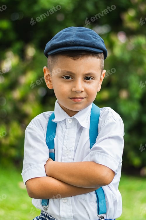 Preview: boy looking serious with his arms crossed, wearing a beret, shirt and trousers with suspenders
