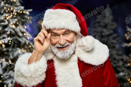 Preview: A cheerful Santa Claus tips his hat while surrounded by magical snow laden evergreen trees