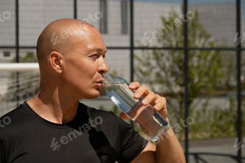 Preview: Athletes man drinking water on outdoor sports ground. Water balance for for active workout.