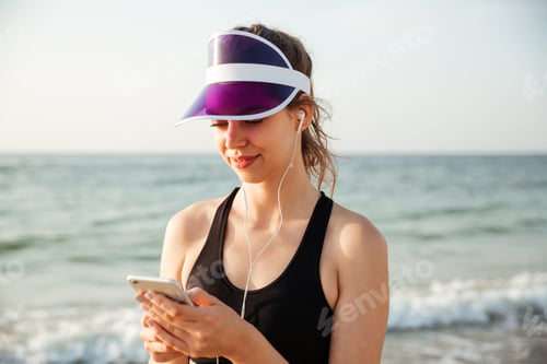 Preview: Fitness woman resting on beach listening to music with phone
