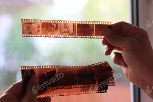 Preview: Anaolog photography on filmstrip. Hands holding photo negatives against the light.