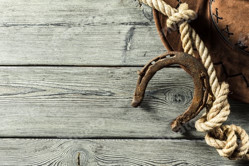 Preview: Horseshoe rests on wooden surface beside rope and cowboy hat during daytime work