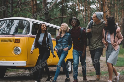 Preview: happy young multiethnic friends traveling together by retro minivan in forest