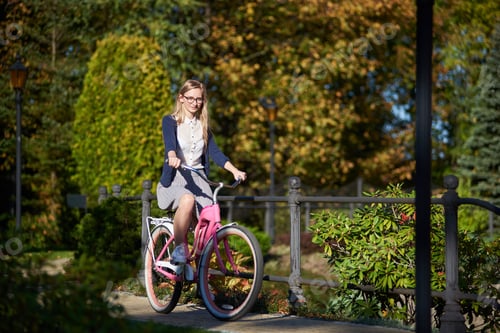 Preview: Blond long-haired attractive girl on pink lady bicycle in sunny autumn park on trees background.