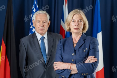 Preview: Two mature political leaders in formalwear standing against four flags