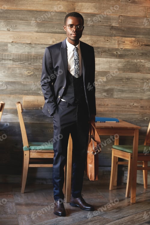 Preview: Full-length portrait of handsome African businessman wearing elegant formal suit, holding leather ba
