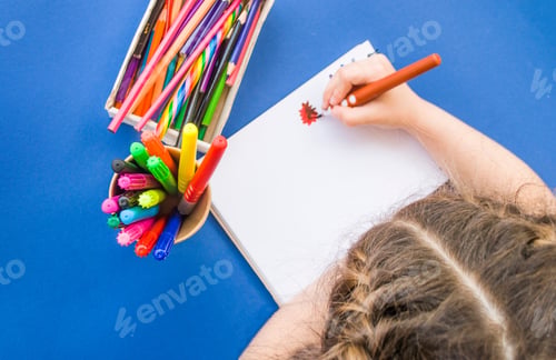 Preview: Child's drawing with colorful pencils and markers in a notebook on blue background with copyspace.