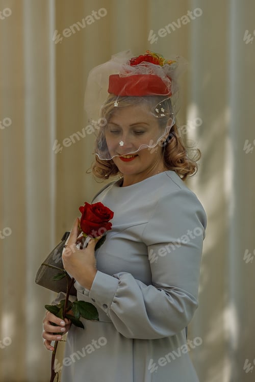 Preview: Young woman in vintage red hat and retro blue dress walking in summer park.