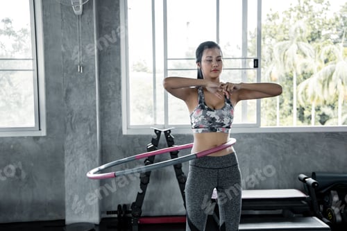 Asian women are exercising with cardio by playing hula hoop in the gym.