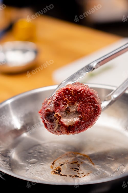 Preview: close-up in a professional kitchen with tongs holding a beef steak over hot frying pan with oil