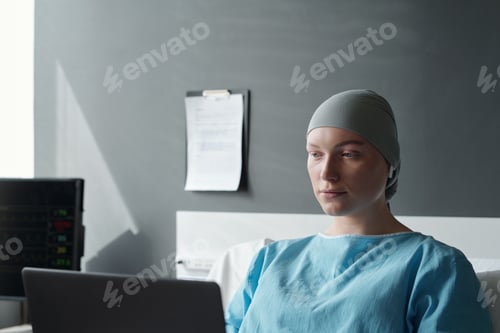 Preview: Young serious woman with oncological disease looking at laptop screen