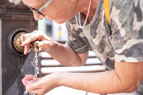 Preview: Close-up view on a mature lady quenching her thirst at the water fountain. Traditional fountain.