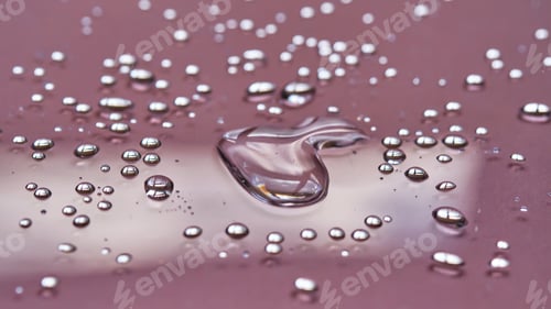 Preview: A large drop and splashes of micellar water on a pink background.