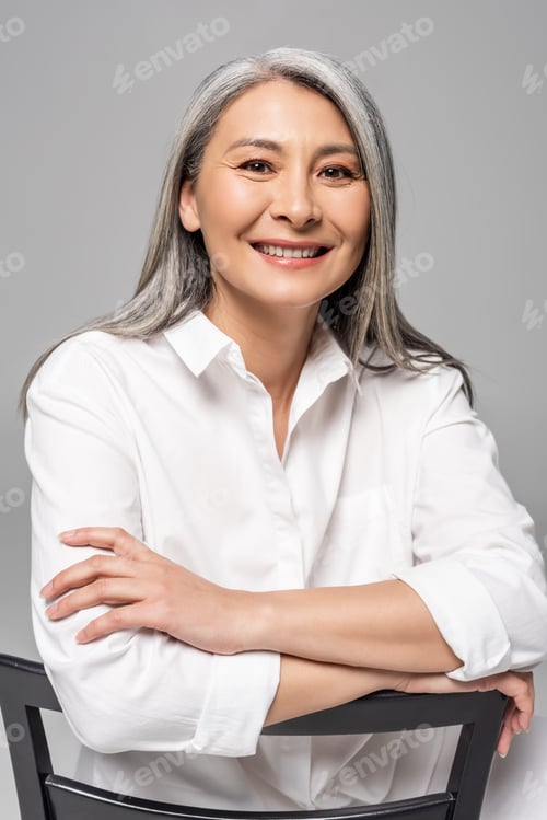 Preview: beautiful smiling asian woman with grey hair sitting on chair isolated on grey