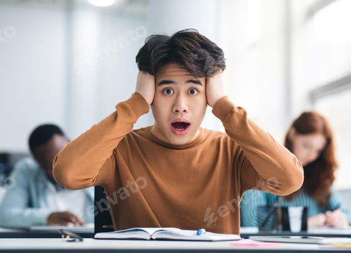 Preview: Asian male student grabbing head sitting at desk in class