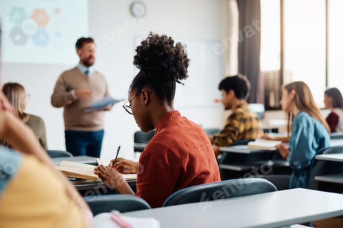 Preview: Black female student taking notes during a class in lecture hall.