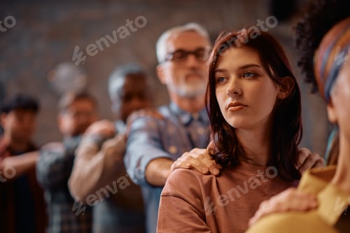Preview: Young pensive woman participating in group therapy at mental health center.