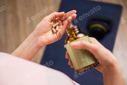 Preview: Human hand with weight loss pills and bottle with blur yoga mat on the floor in the background