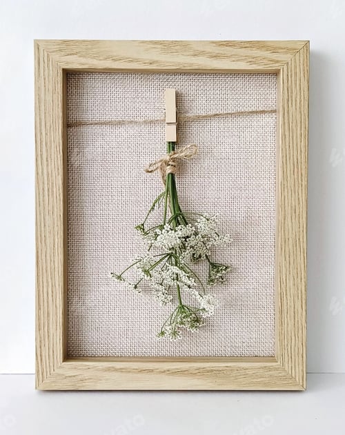 Preview: Bouquet of white flowers hanging on clothespin in wooden frame on light background