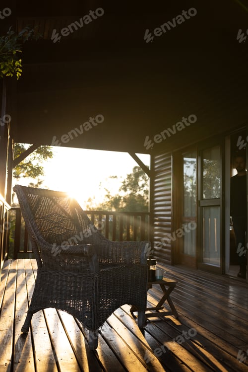 Preview: Vertical image of balcony of log cabin with armchair and mug of coffee on sunny day