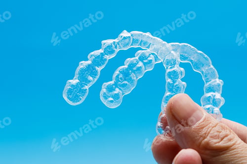 Preview: Hand holding two transparent retainers on blue background. Invisalign orthodontics concept