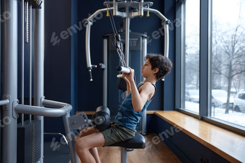 Preview: Cute preteen boy training muscle at gym machine pulling down bar