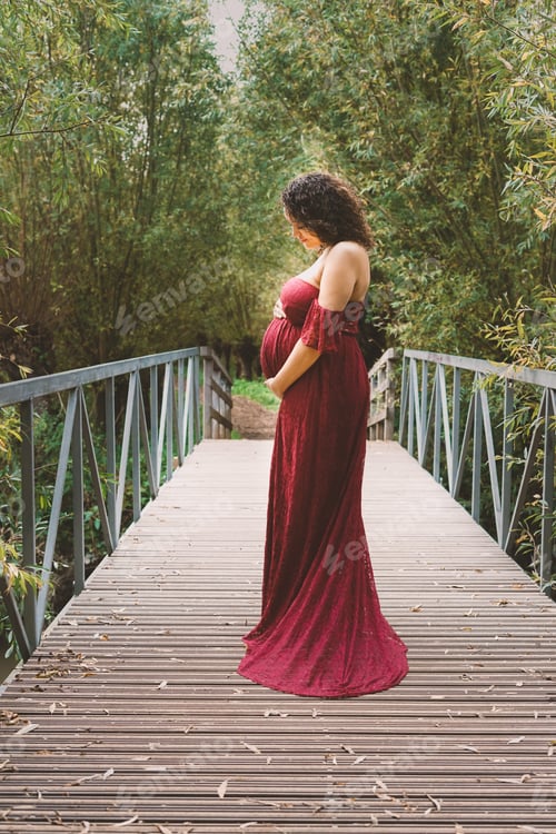 Preview: Beautiful pregnant afro woman hugging her tummy, enjoying her pregnancy, outdoors