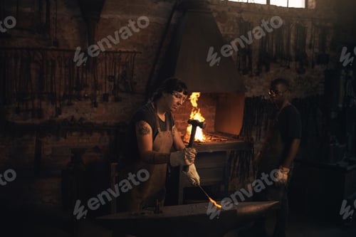 Preview: Shot of a young woman hitting a hot metal rod with a hammer in a foundry