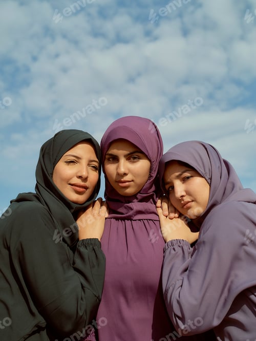 Preview: Three women in colorful hijabs standing close together under a blue sky with clouds, Morocco