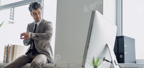 Preview: Handsome young man checking the time while sitting on the window sill in office