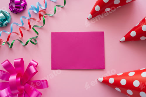 Preview: Top view of empty greeting card near serpentine and party caps on pink background