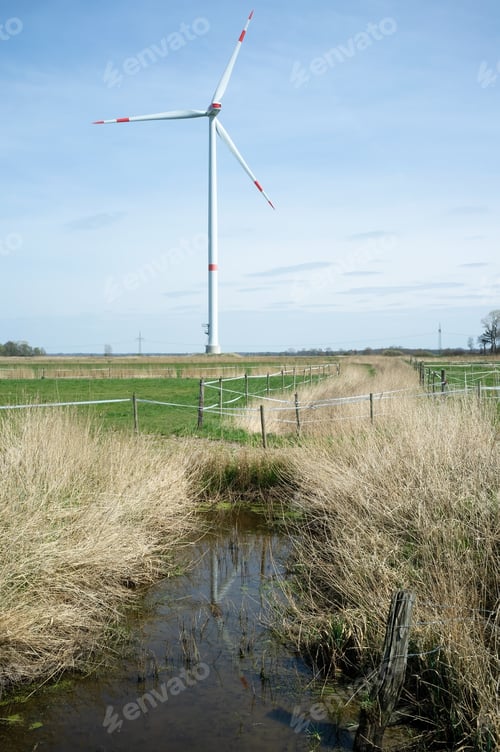 Preview: Wind turbine in a field divided by a ditch filled with water, in countryside. Clean energy concept