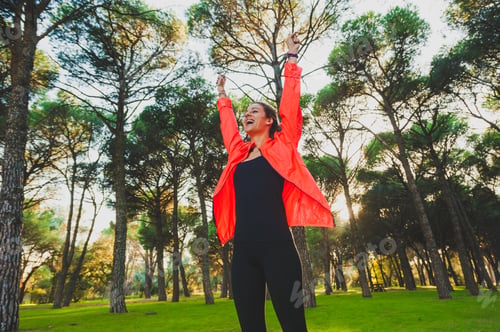 Preview: Excited sportswoman with arms raised in park