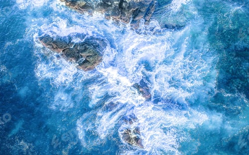 Preview: Drone shot top down of blue ocean waves crashing over rocks along the coast