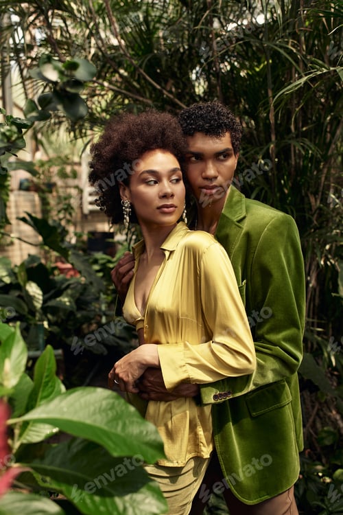 Preview: Young couple embraces amidst lush greenery in a vibrant greenhouse setting
