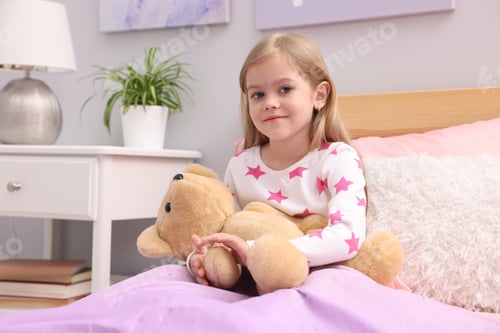 Preview: Cute little girl with teddy bear on bed at home