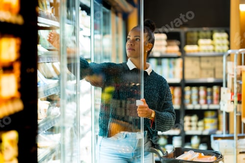 Preview: Woman choosing food from refrigerated display in supermarket