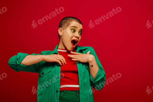 Preview: fashion statement, amazed and tattooed, short haired woman in green outfit touching chest on red