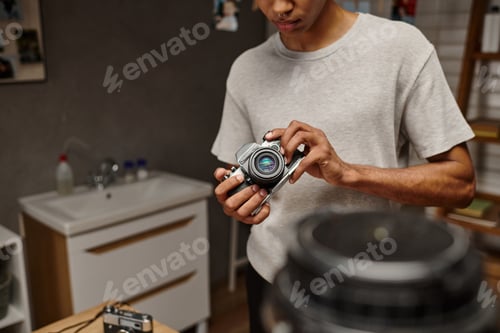 Preview: cropped view of young african american photographer expertly handling a vintage camera in photo lab