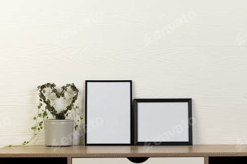 Preview: Black empty frames with copy space and heart shape plant on table against white wall