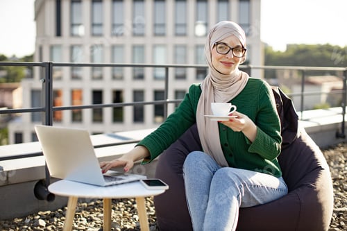 Preview: Arabian woman with device drinking coffee on roof terrace