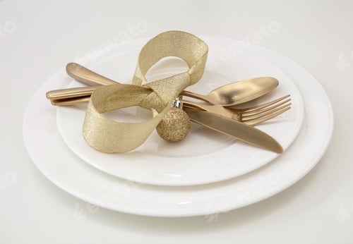 Preview: Christmas table setting close up. Golden cutlery and decoration on white dishes,