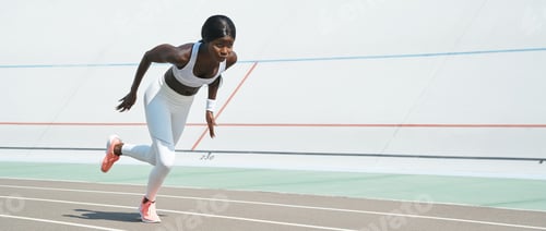 Preview: Confident young African woman in sports clothing running on track outdoors