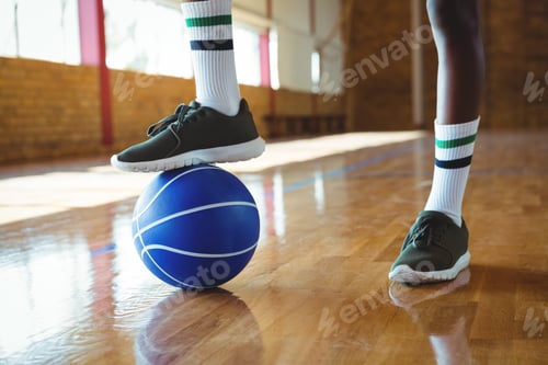 Preview: Low section of teenage boy stepping on basketball